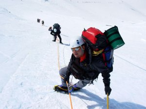 A climber ascends Mt. McKinley with a green "clean mountain can" (CMC) strapped to his backpack (image from Coley Gentzel, National Park Service).